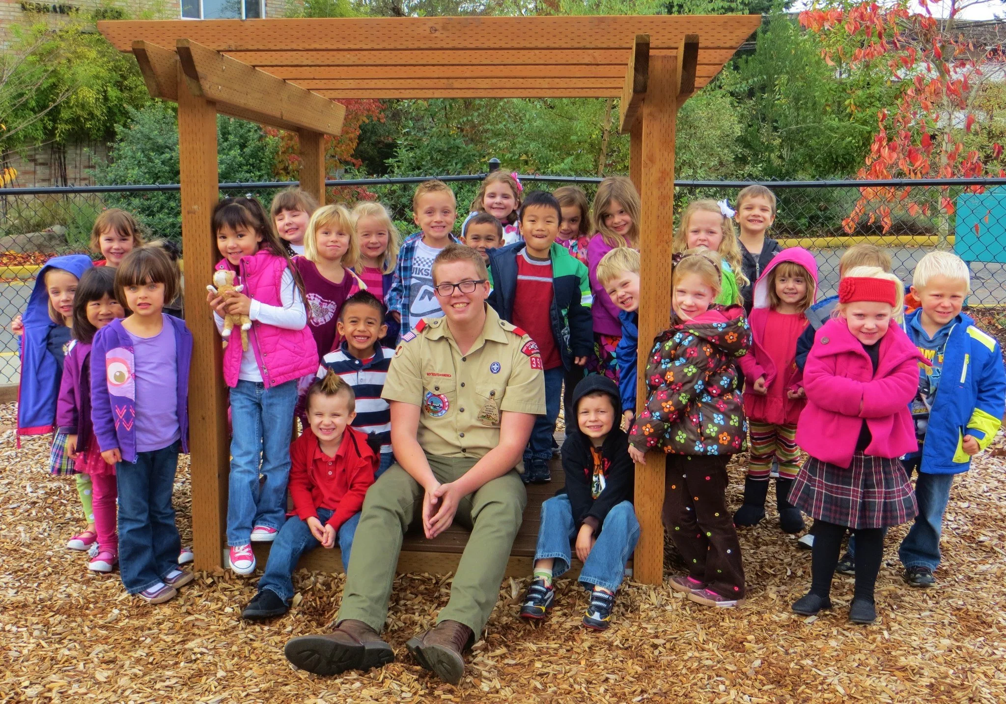 Zach in his Scout uniform with children gathered beneath a wooden pergola